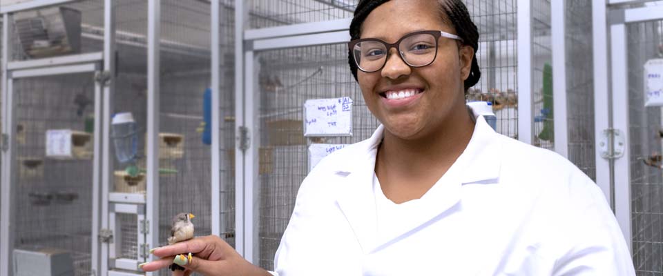 Person in lab coat with a bird perched on her finger