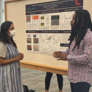 A photo of Jared Barnes (right), a senior biology major from Grenada, talks about his biodegradable drug delivery system research during a poster presentation for the UM Summer Undergraduate Research Group Grant program. Photo by Shea Stewart/UM Office of Research and Sponsored Programs